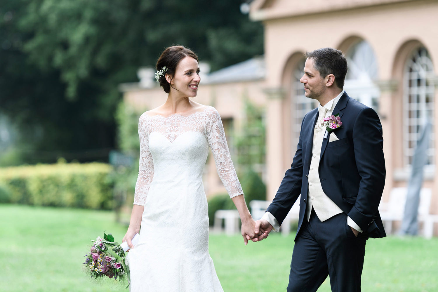 Hochzeitspaar geht im Park von Schloss Heeren Hand in Hand