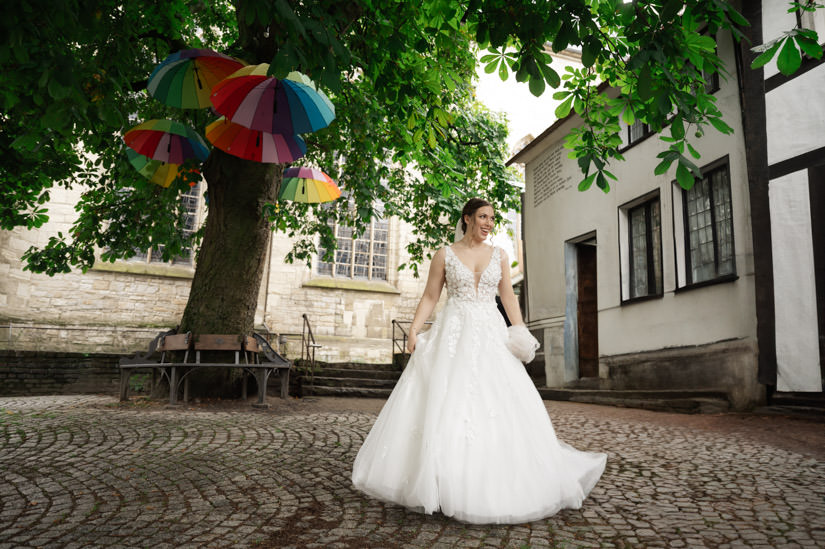 Braut steht vor dem Nicolaihaus mit bunten Regenschirmen im Hintergrund