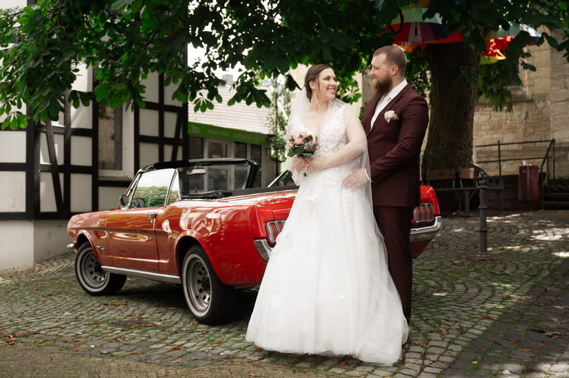 Brautpaar steht vor rotem Auto
