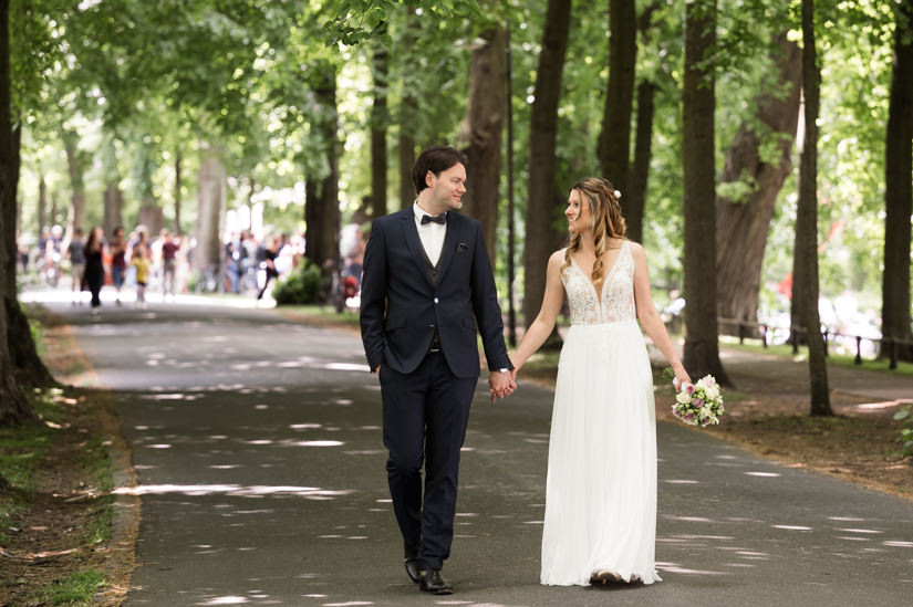 Hochzeitspaar geht Hand in Hand auf der Promenade in Münster spazieren