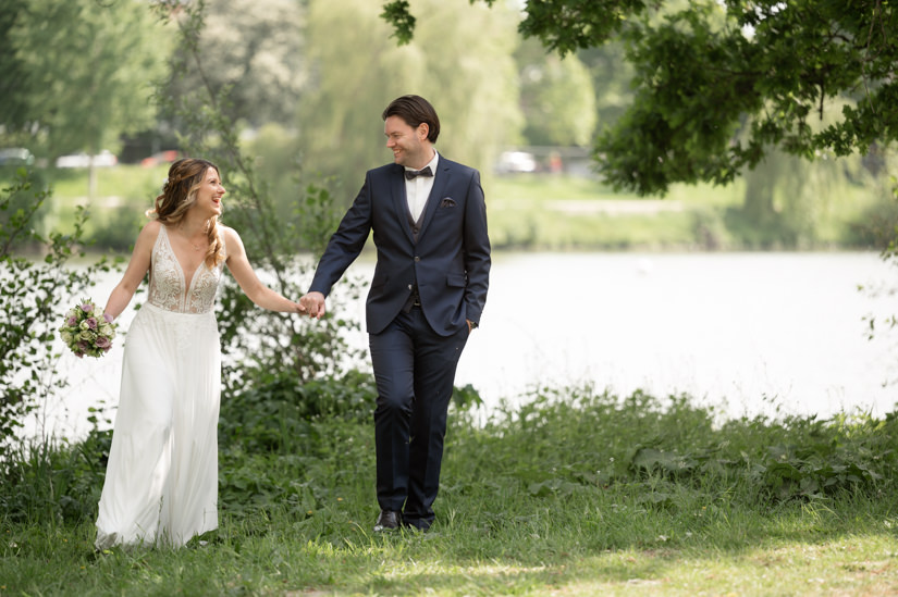 Hochzeitspaar geht am Ufer des Aasees in Münster spazieren