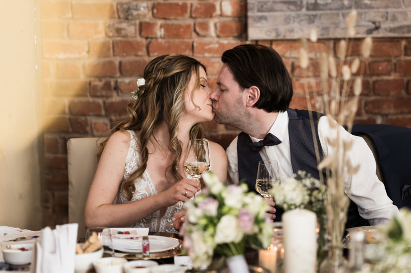 Braut und Bräutigam küssen sich am Tisch